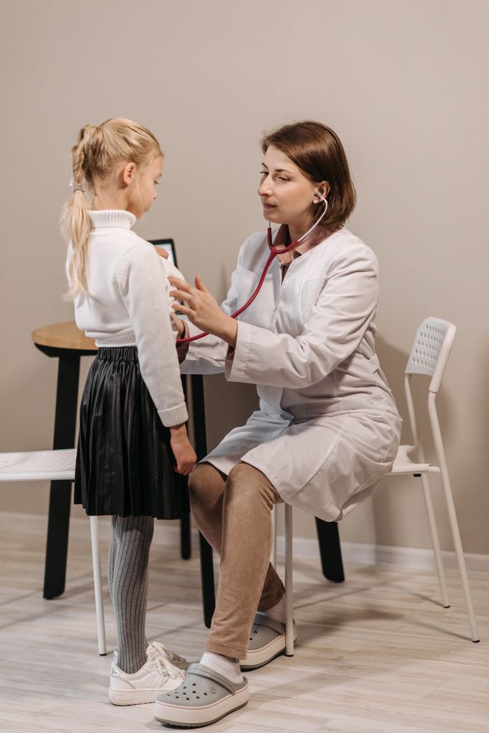 A healthcare worker examining a child with a stethoscope in a clinic setting.